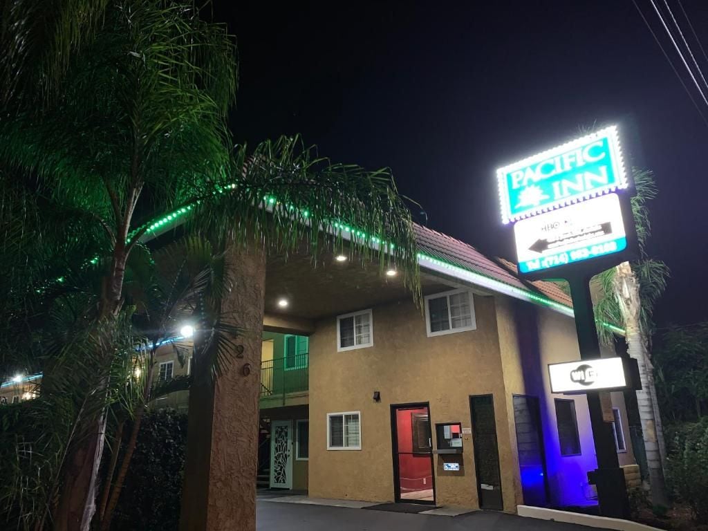 A Pacific Inn hotel with a neon sign, a visible entrance, and a palm tree in the foreground.