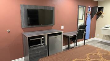 A hotel room with a bed, a desk with a computer, a microwave, and a television.