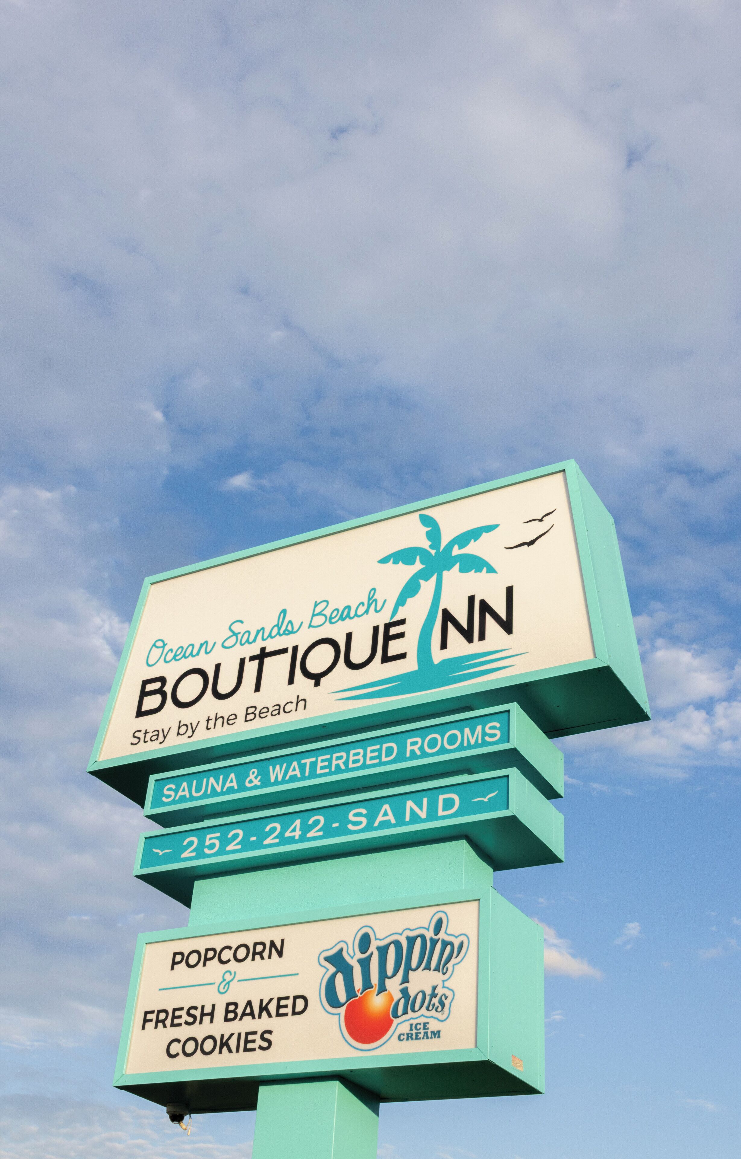 A sign for Ocean Sands Boutique Inn with amenities like sauna, waterbed rooms, and a contact number.