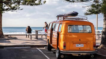 A vintage orange van parked by the seaside with a clear view of the ocean.