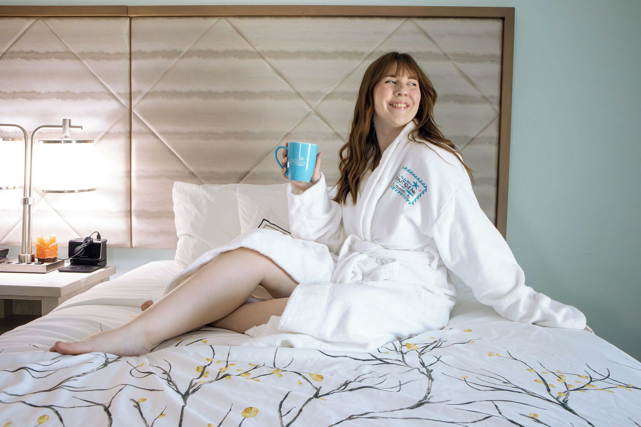 Iemand zit op een bed in een hotelkamer en houdt een blauwe mok vast.