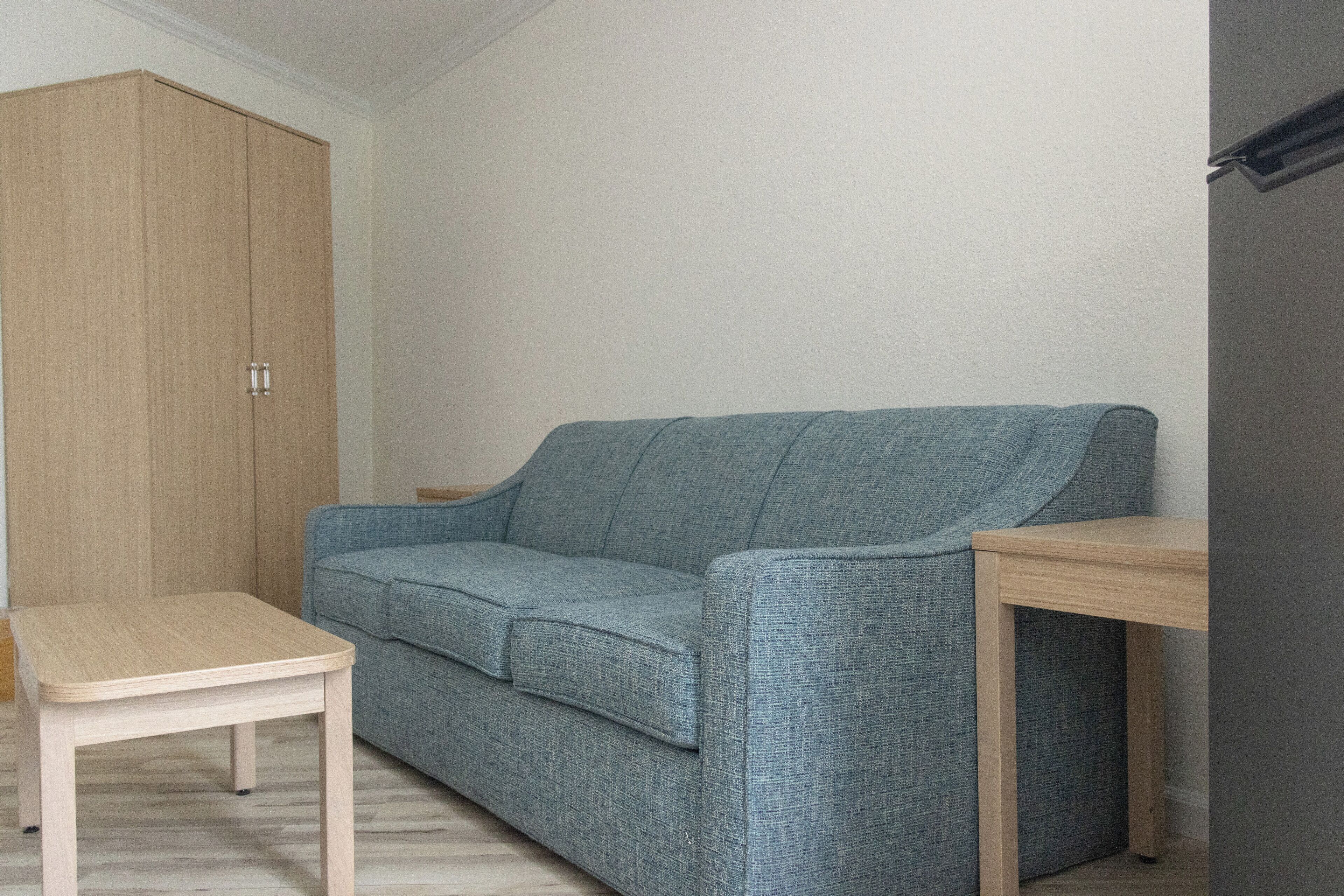 Une pièce avec une armoire en bois clair, un canapé gris et une petite table en bois.