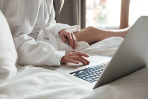 A person using a laptop on a bed with white bedding.