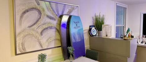 A hotel reception area with a large abstract painting, a blue and white decor piece, a small plant, and a table with a book and a vase of flowers.