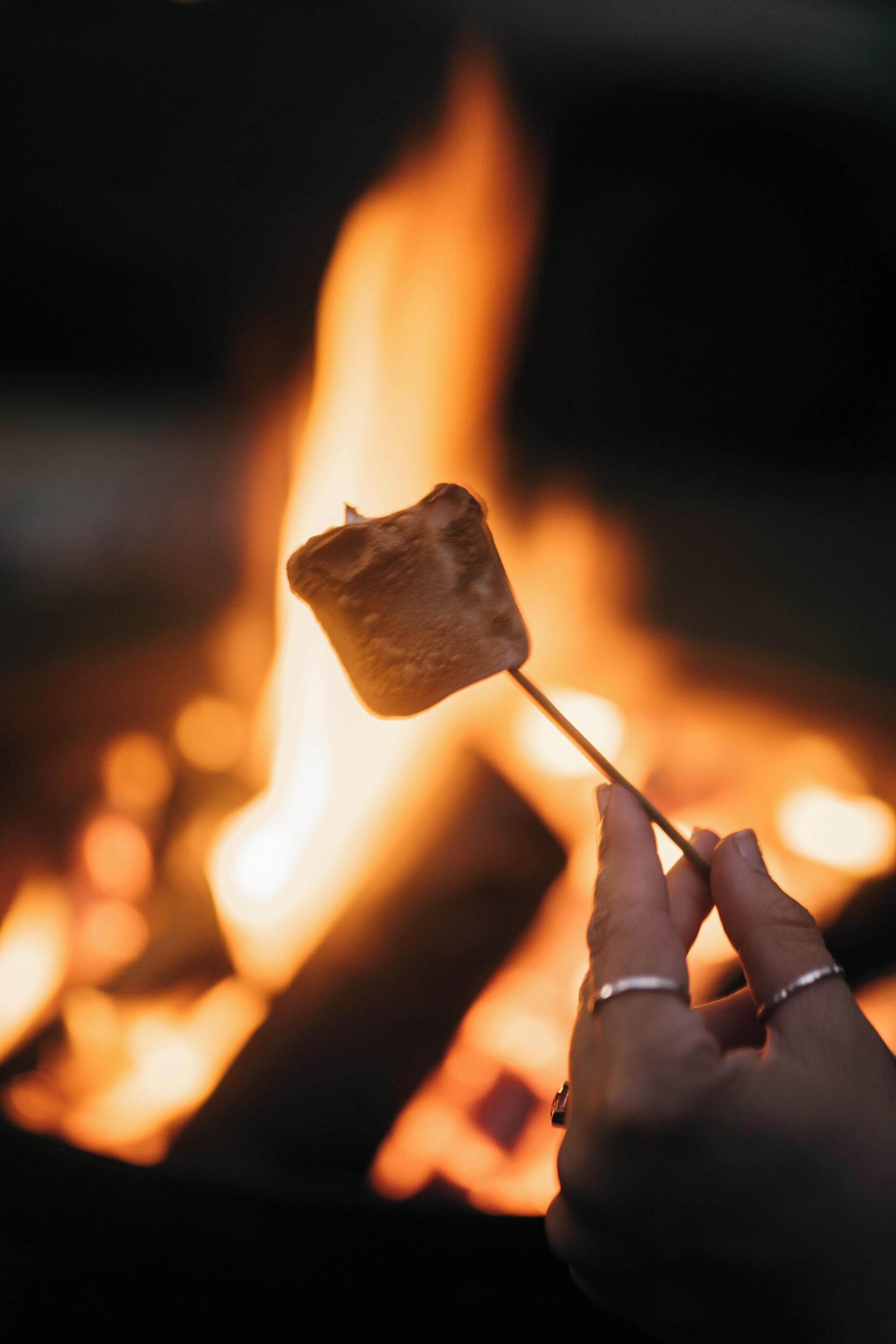 A hand holding a marshmallow over a fire.