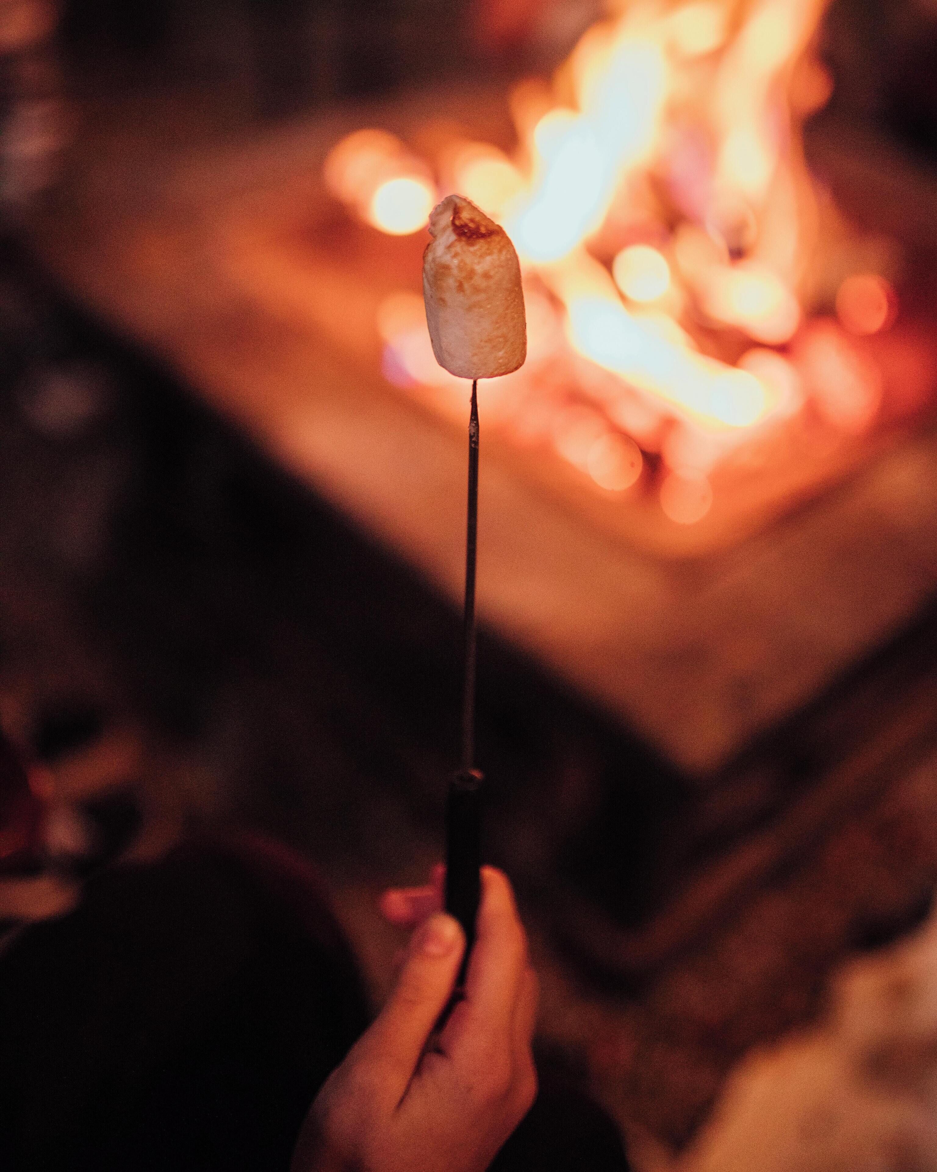 Una persona sosteniendo un pincho con malvavisco sobre una fogata.