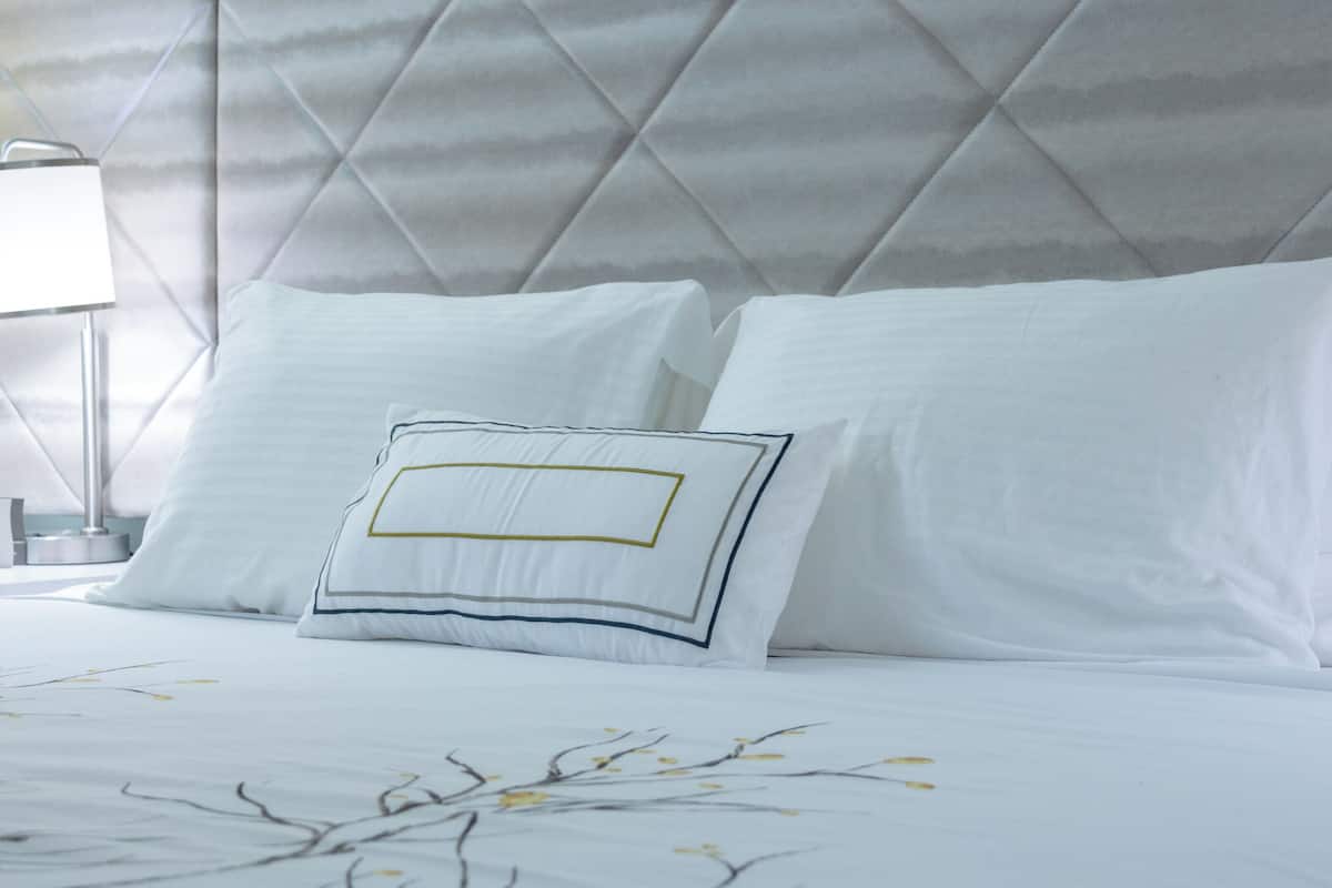 A neatly made bed with white linens and a decorative pillow with a geometric design.
