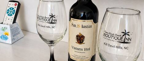A bottle of Vintners Red wine, two glasses with the Boutique Inn logo, and a remote control on a counter.