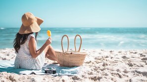 A person sitting on a beach towel with a camera and a basket, overlooking the ocean. - Ocean Sands Beach Boutique Inn - Stay At the Beach (Kill Devil Hills)
