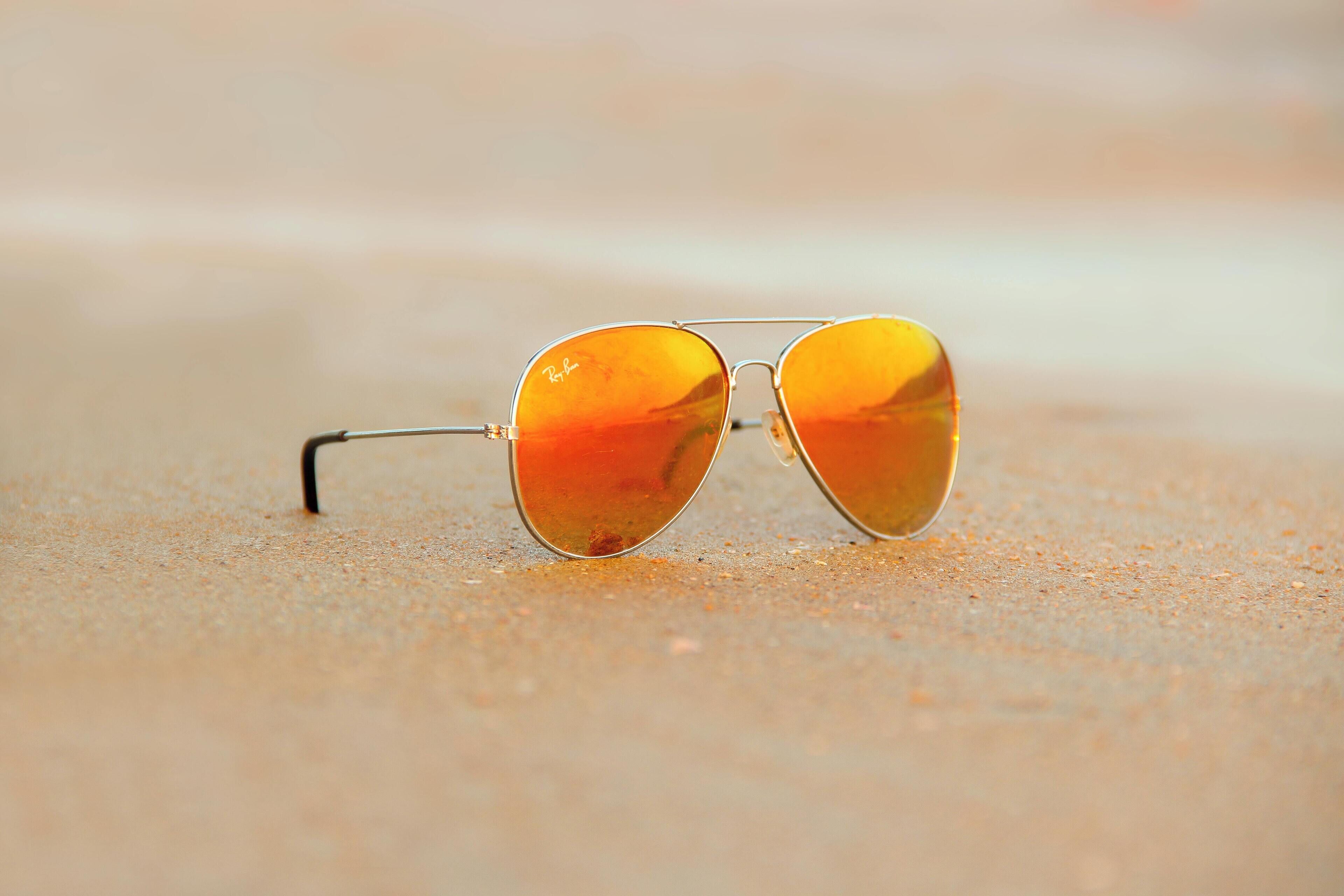 Une paire de lunettes de soleil avec une monture métallique et des verres réfléchissants, posée sur une surface sablonneuse.