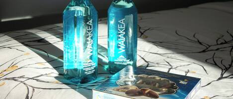 Two bottles of Hawaiian Volcanic Water on a bed with a patterned bedspread and a box of nuts.