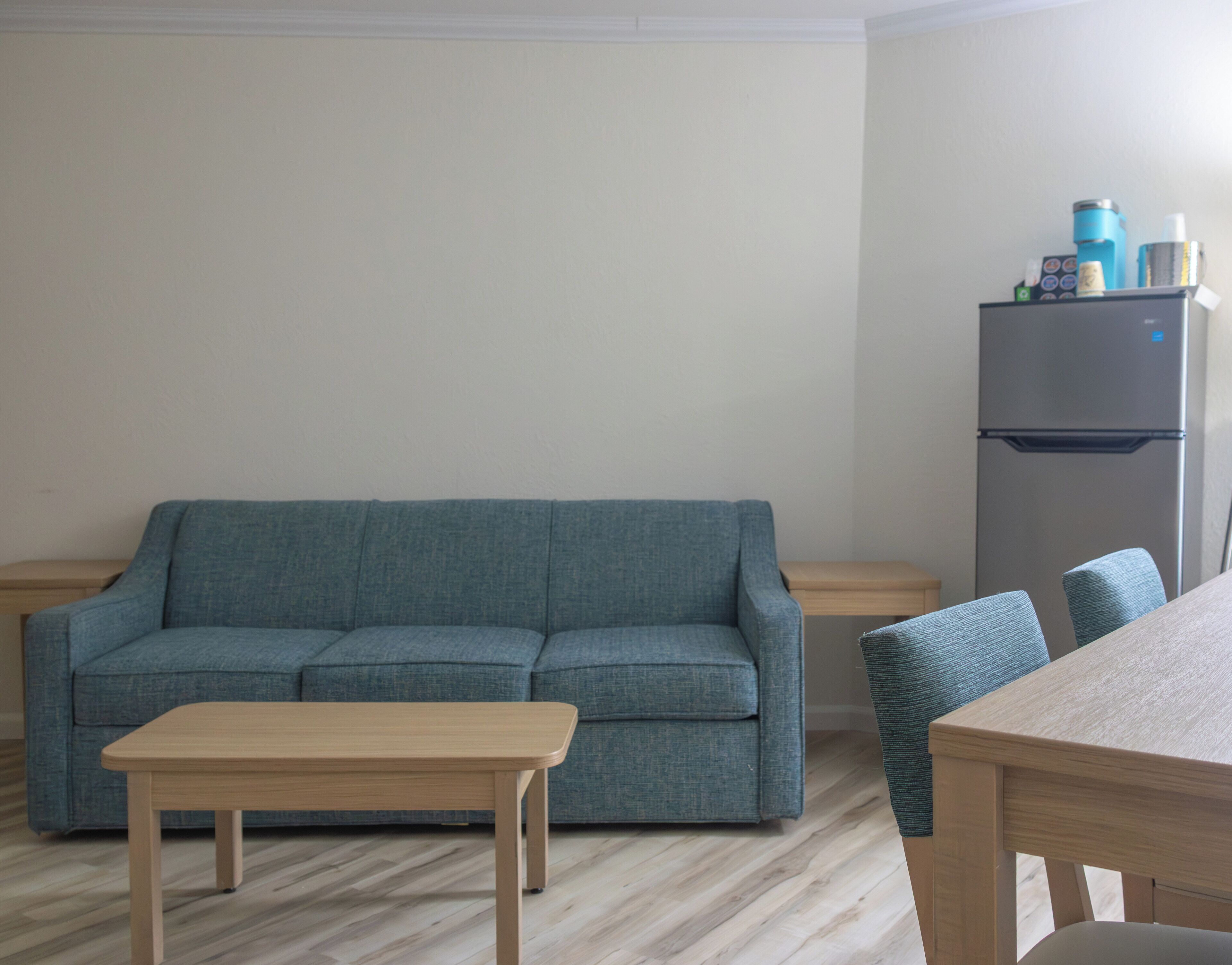 Una sala de estar con un sofá, una mesa de madera y un refrigerador.
