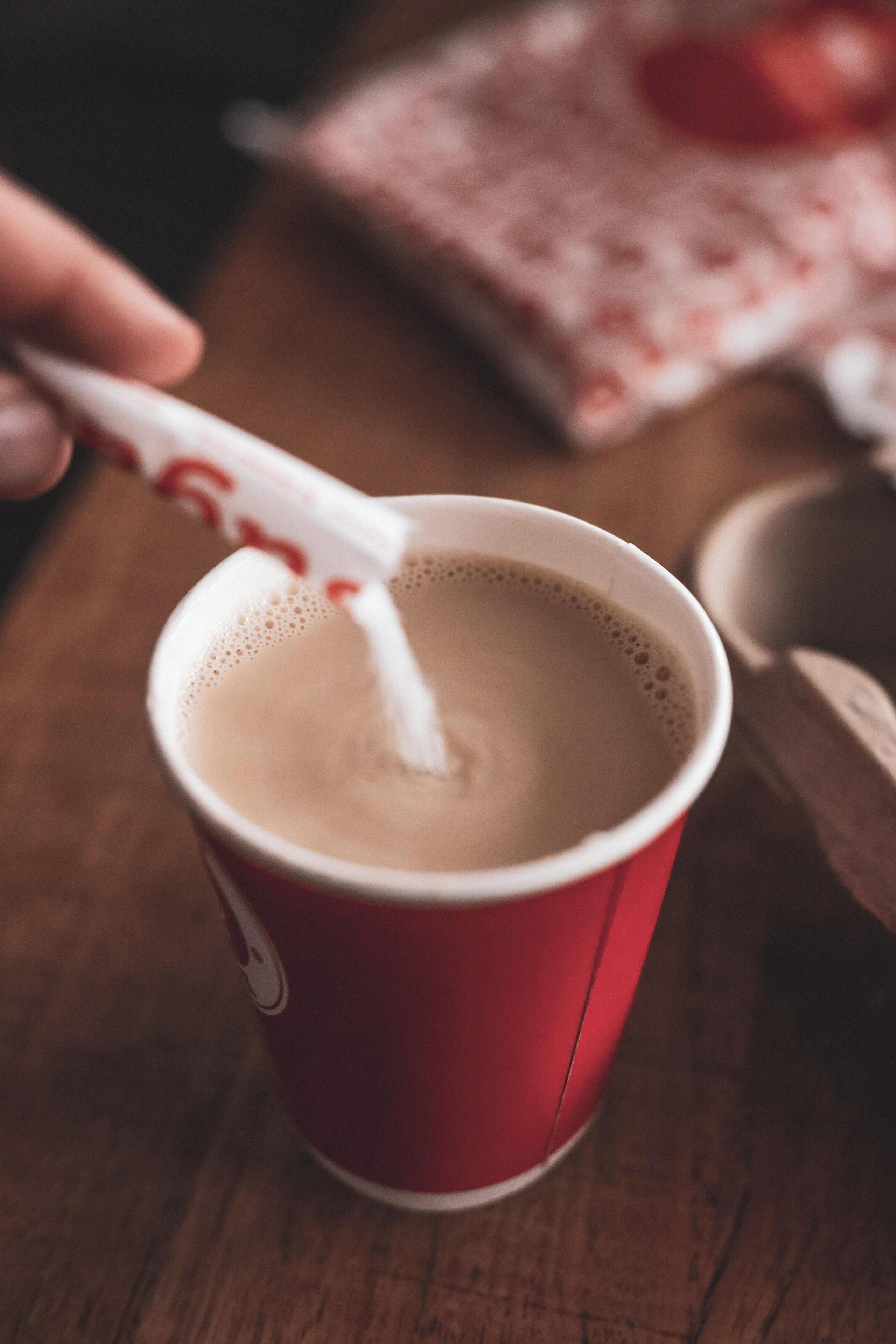 Une tasse de café rouge avec une cuillère, posée sur une table en bois.