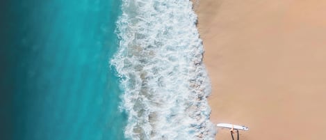 Eine Vogelperspektive eines Strandes, auf dem eine Person ein Surfbrett hält.