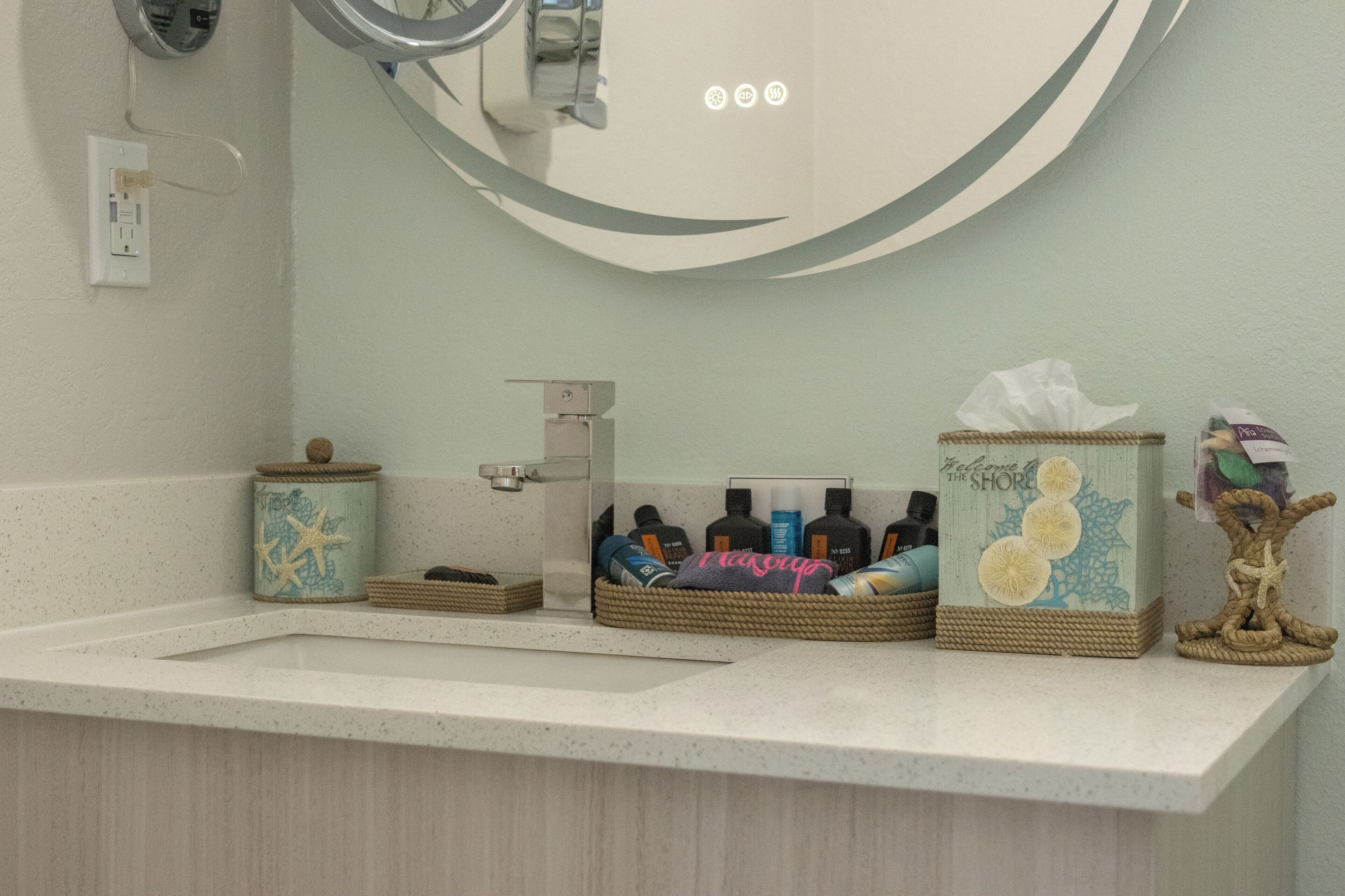 A bathroom with a white countertop, a mirror, and three wicker baskets containing toiletries.