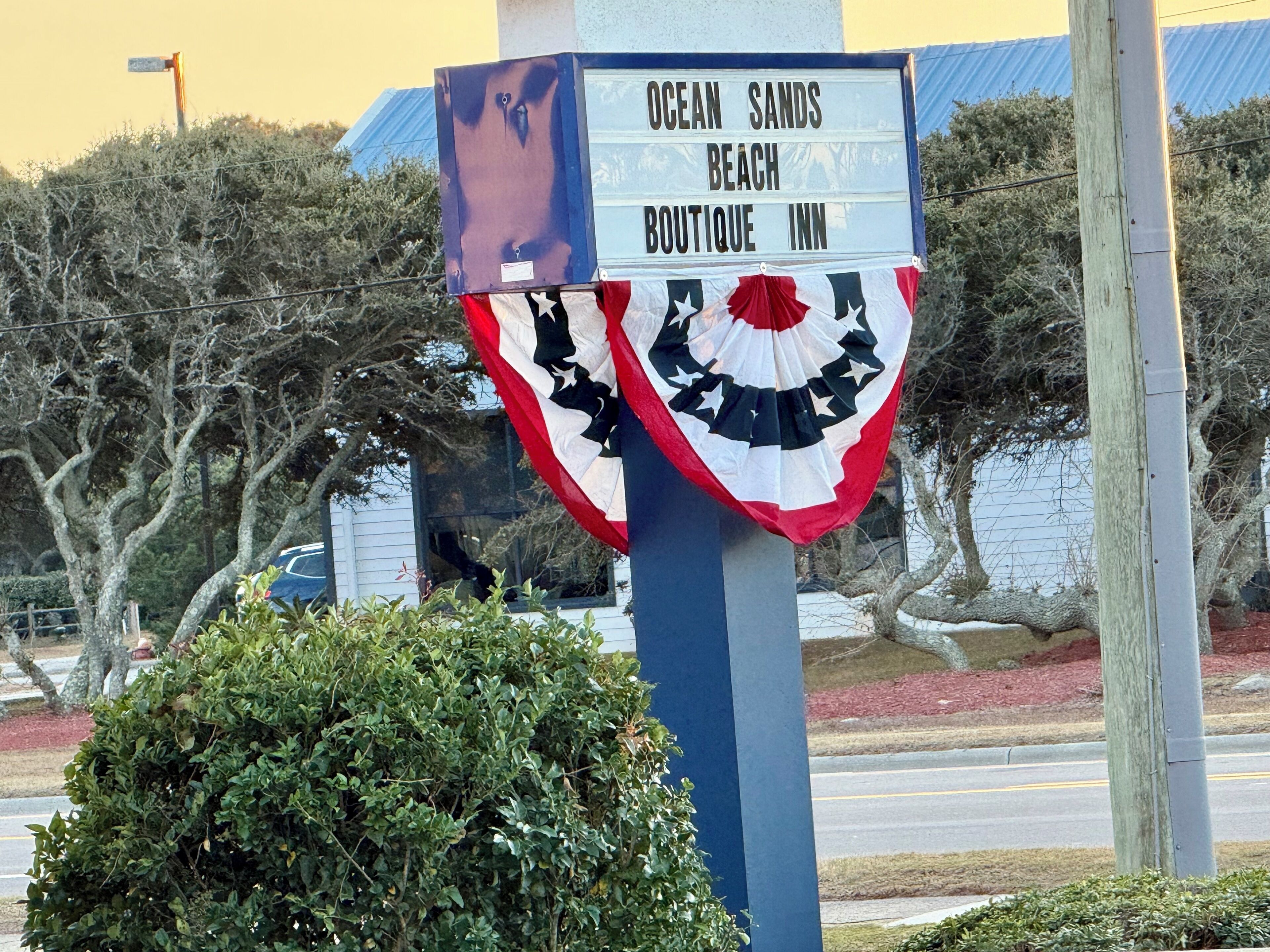 A sign for Ocean Sands Beach Boutique Inn with a flag decoration.