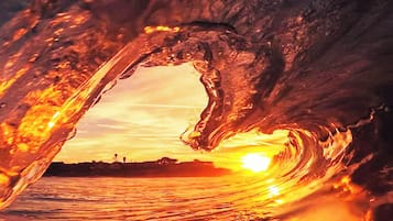 Un atardecer visto a través de la cresta de una ola, con el sol parcialmente oculto por el agua.