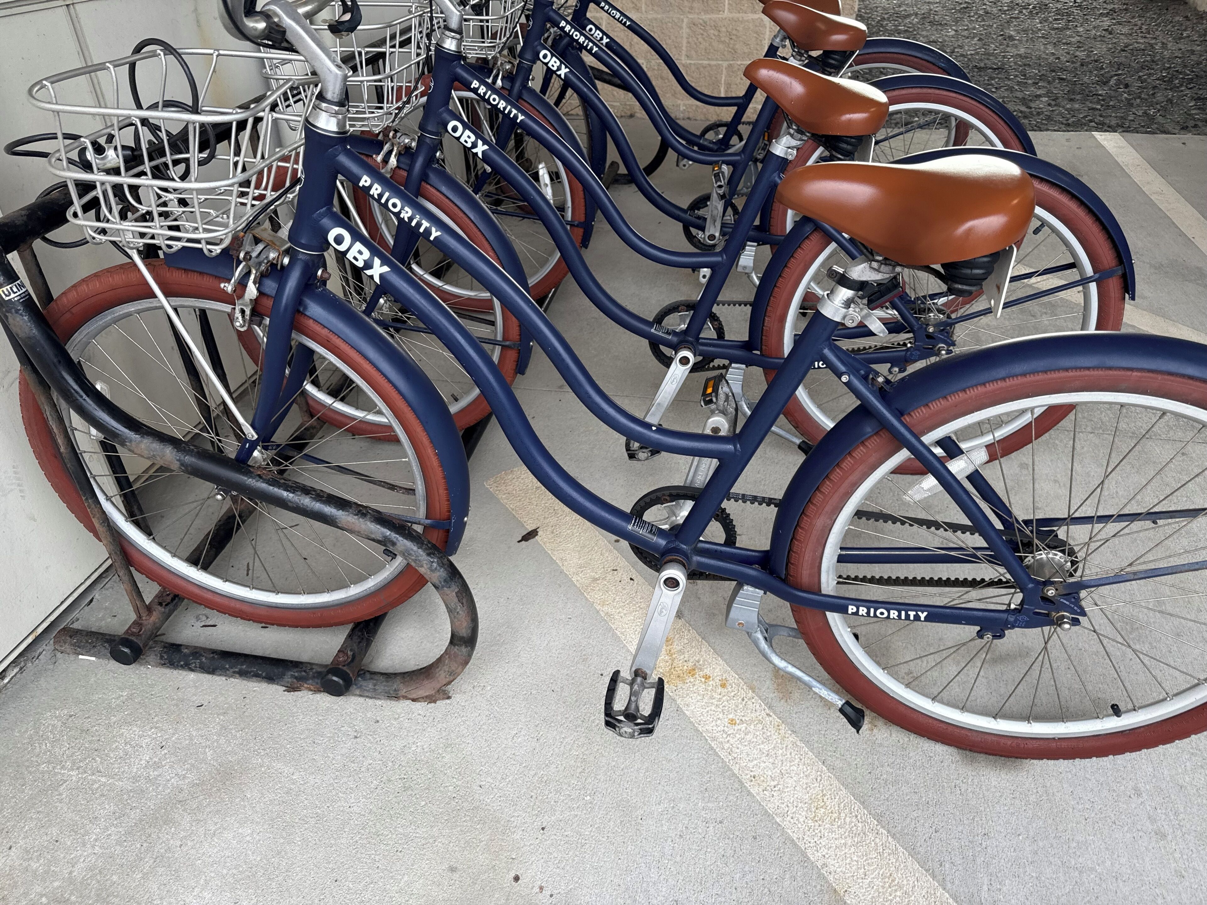 Una hilera de bicicletas con las etiquetas 'OBX' y 'PRIORITY', estacionadas en un área designada.