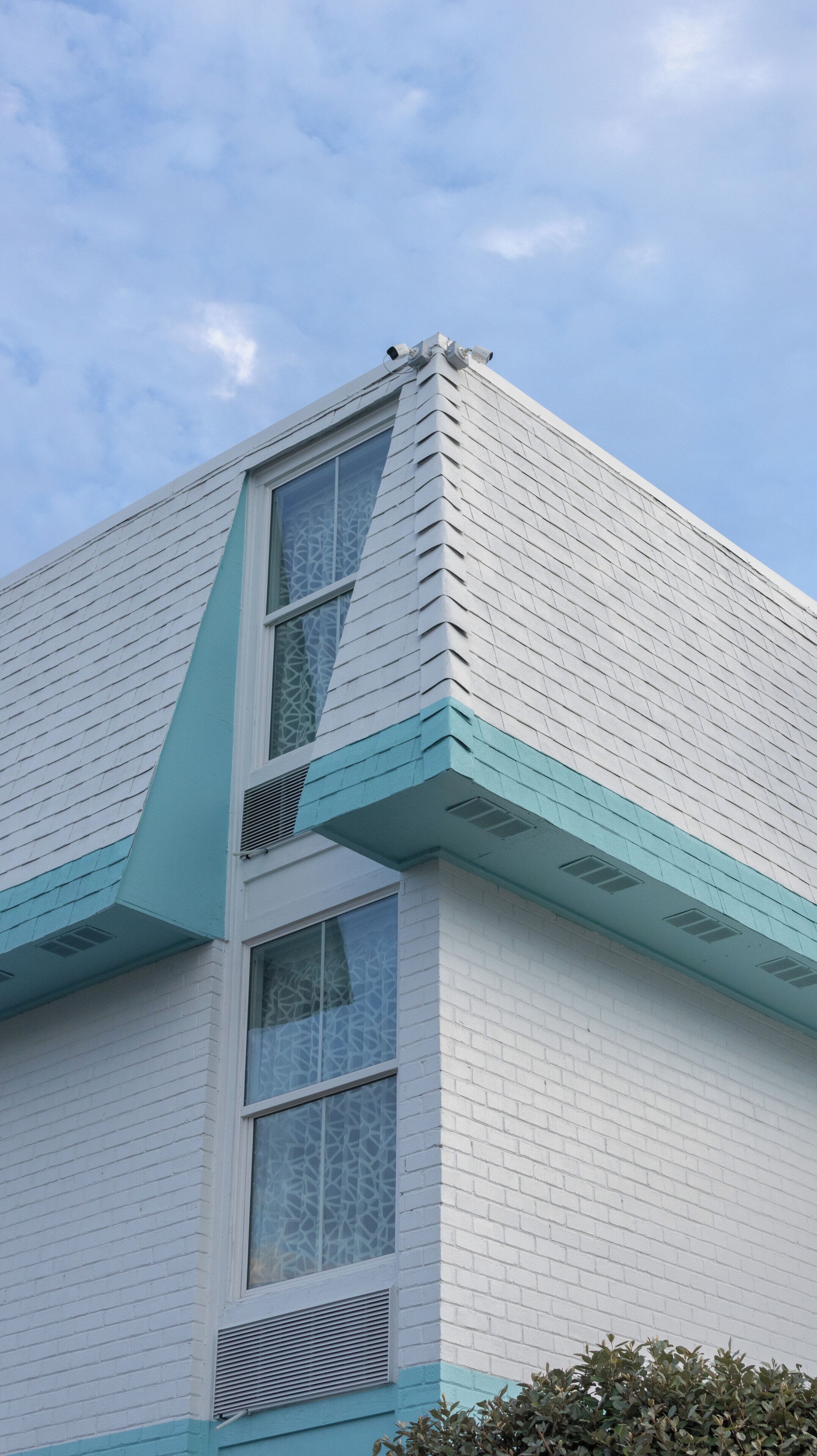 A corner of a building with white siding and teal trim, featuring a window with a patterned glass design.
