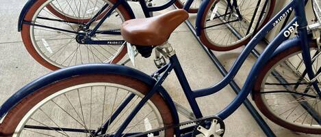 Una bicicleta azul con asiento marrón y la palabra 'PRIORITY' escrita en el cuadro, estacionada junto a otra bicicleta.