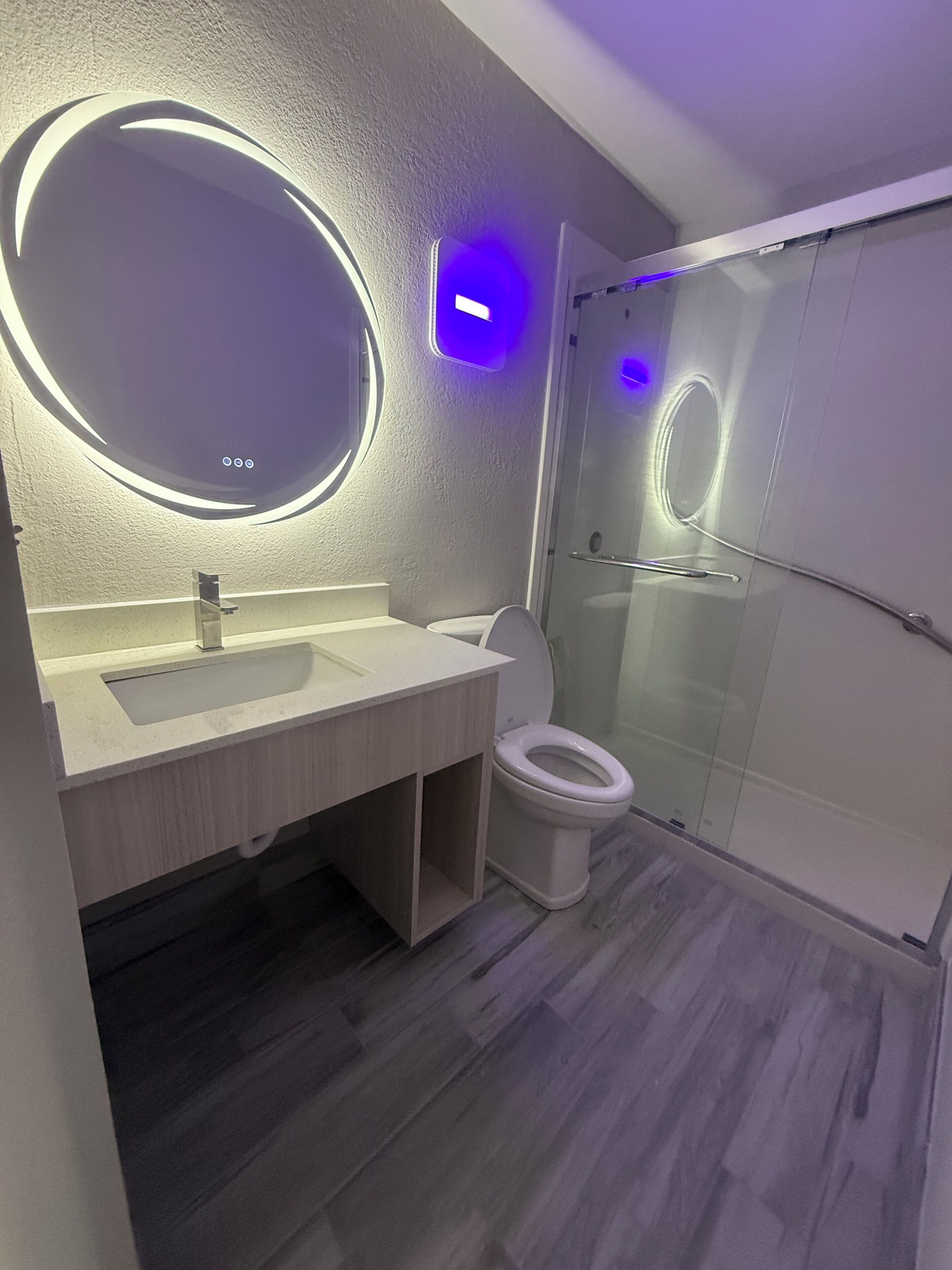 Een moderne badkamer met een ronde spiegel, toilet en een douchecabine van glas.