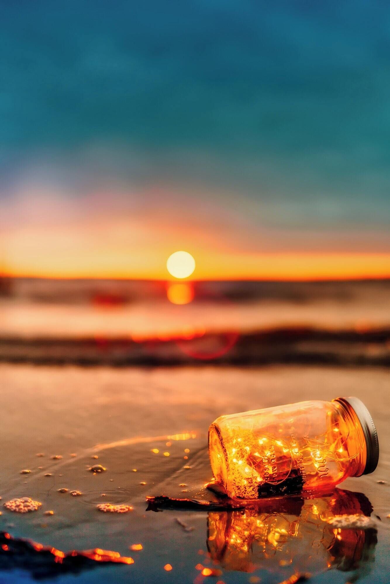 A sunset over a beach with a glass bottle tipped over, spilling its contents.