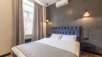 A modern hotel room with a large bed, a brick-patterned wall, and a window with curtains.