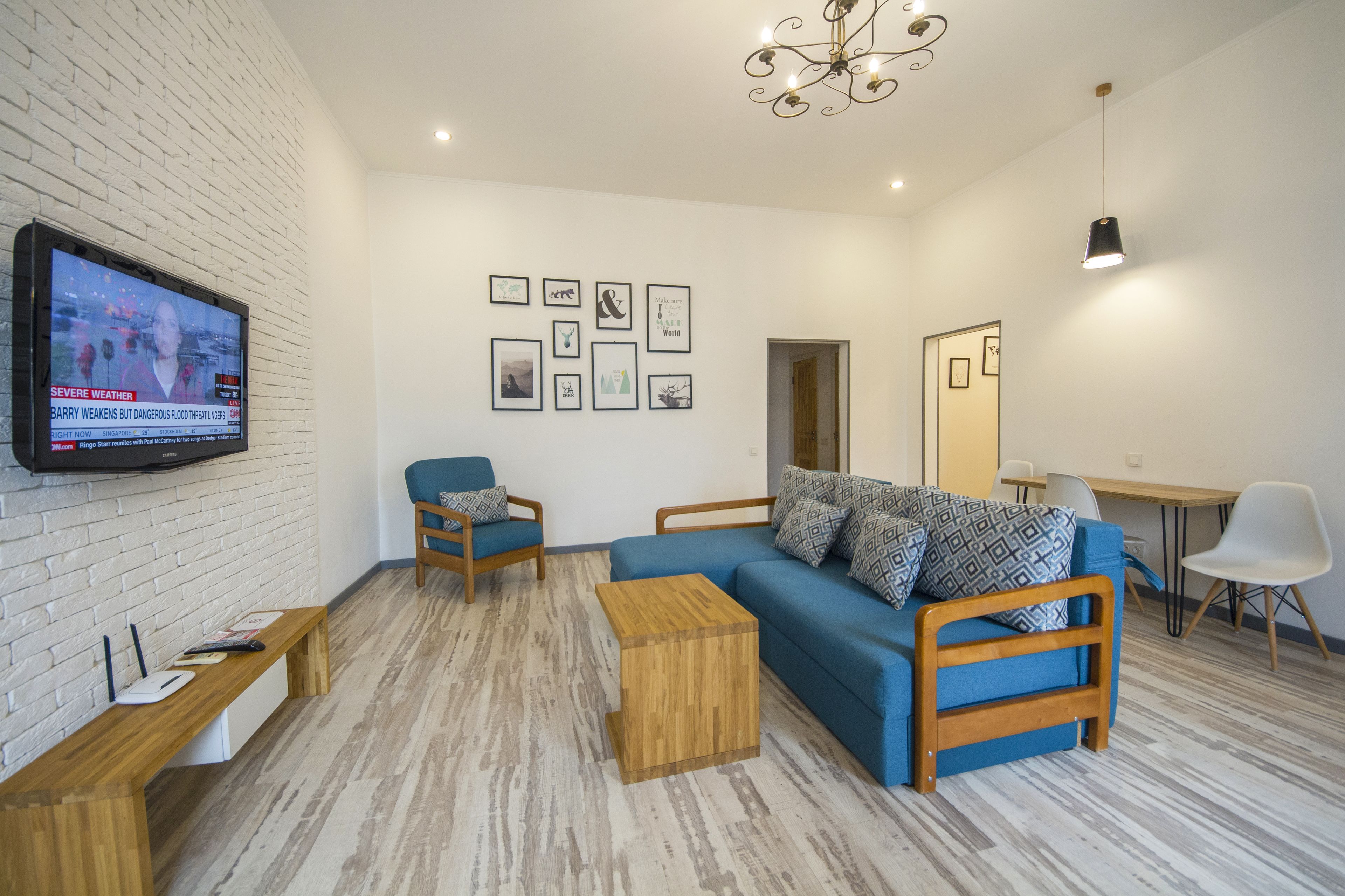 Un salon moderne avec un canapé bleu, une table basse en bois et un téléviseur à écran plat fixé à un mur en briques.