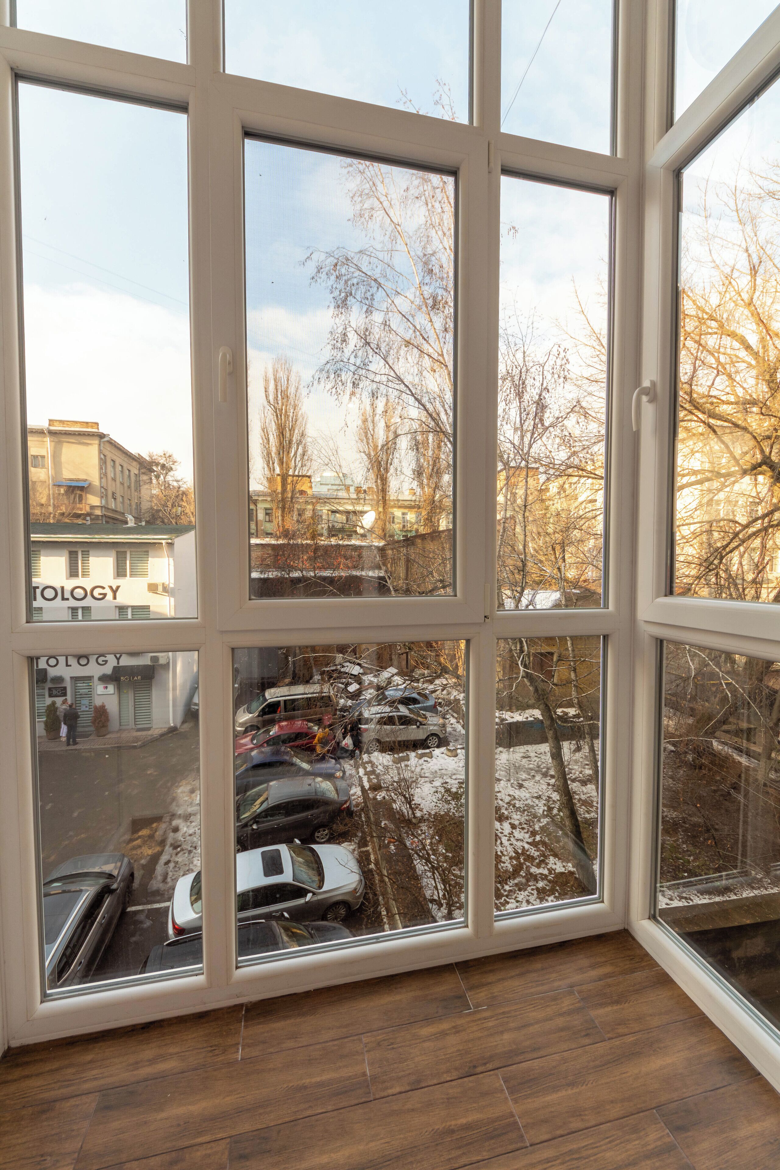 Una habitación con ventanas amplias que dan a un estacionamiento y edificios.