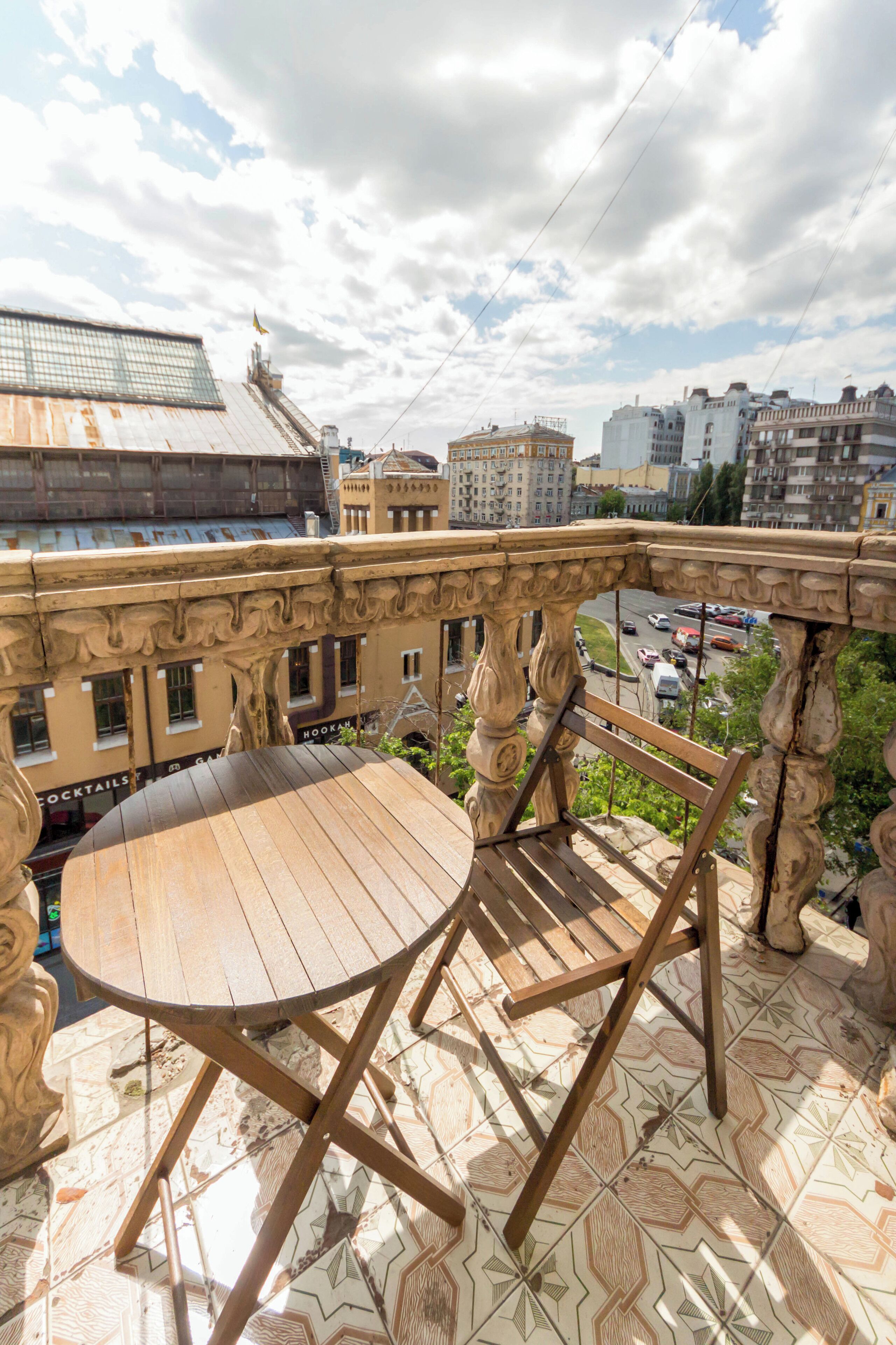 Varanda com mesa e cadeiras de madeira, com vista para um horizonte urbano com edifícios e rua.