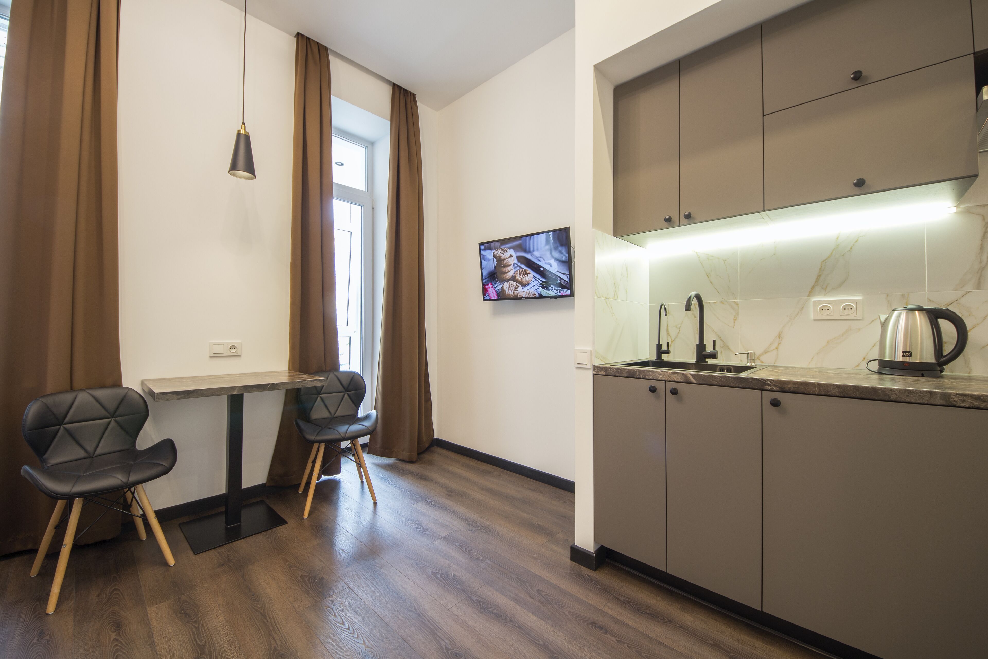 Eine moderne Küche mit Marmorarbeitsplatte, einem Wasserkocher und einem an der Wand befestigten Fernseher.