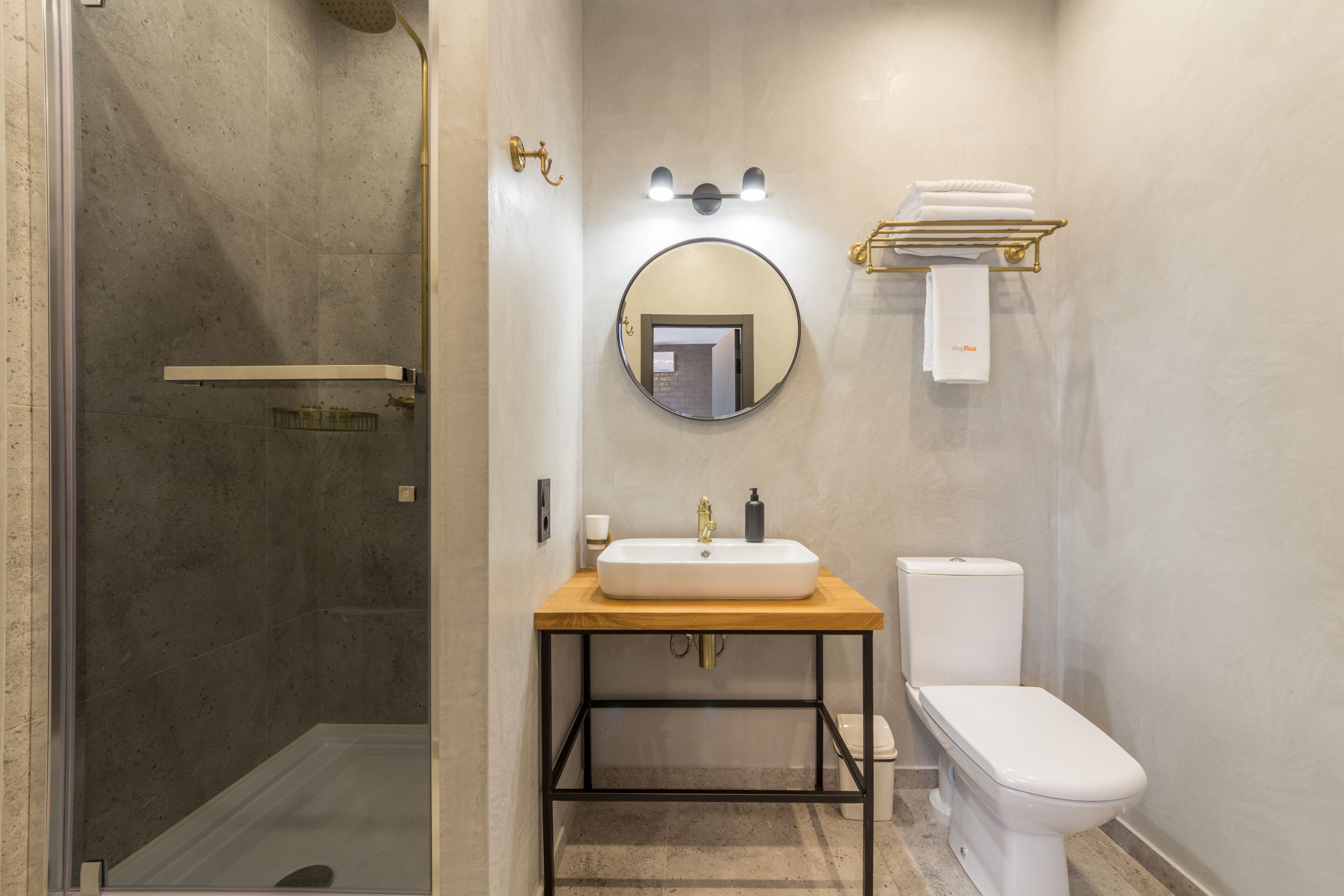 A modern bathroom with a glass-enclosed shower, a round mirror, a sink with a wooden countertop, and a toilet.
