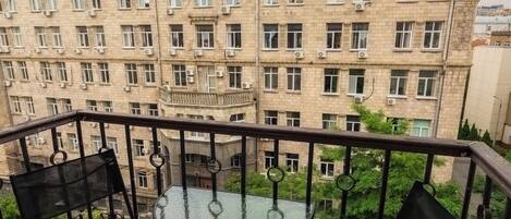 Un balcon avec une table en verre et deux chaises, donnant sur un immeuble doté de nombreuses fenêtres et de balcons.