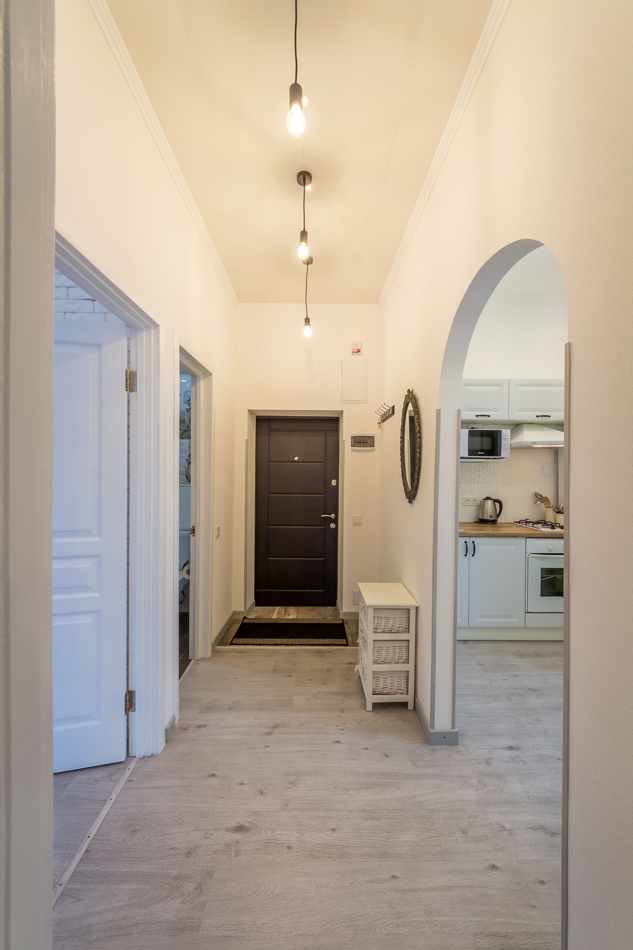A hallway with a dark door, a white bench, and a kitchen area with white cabinets and appliances.