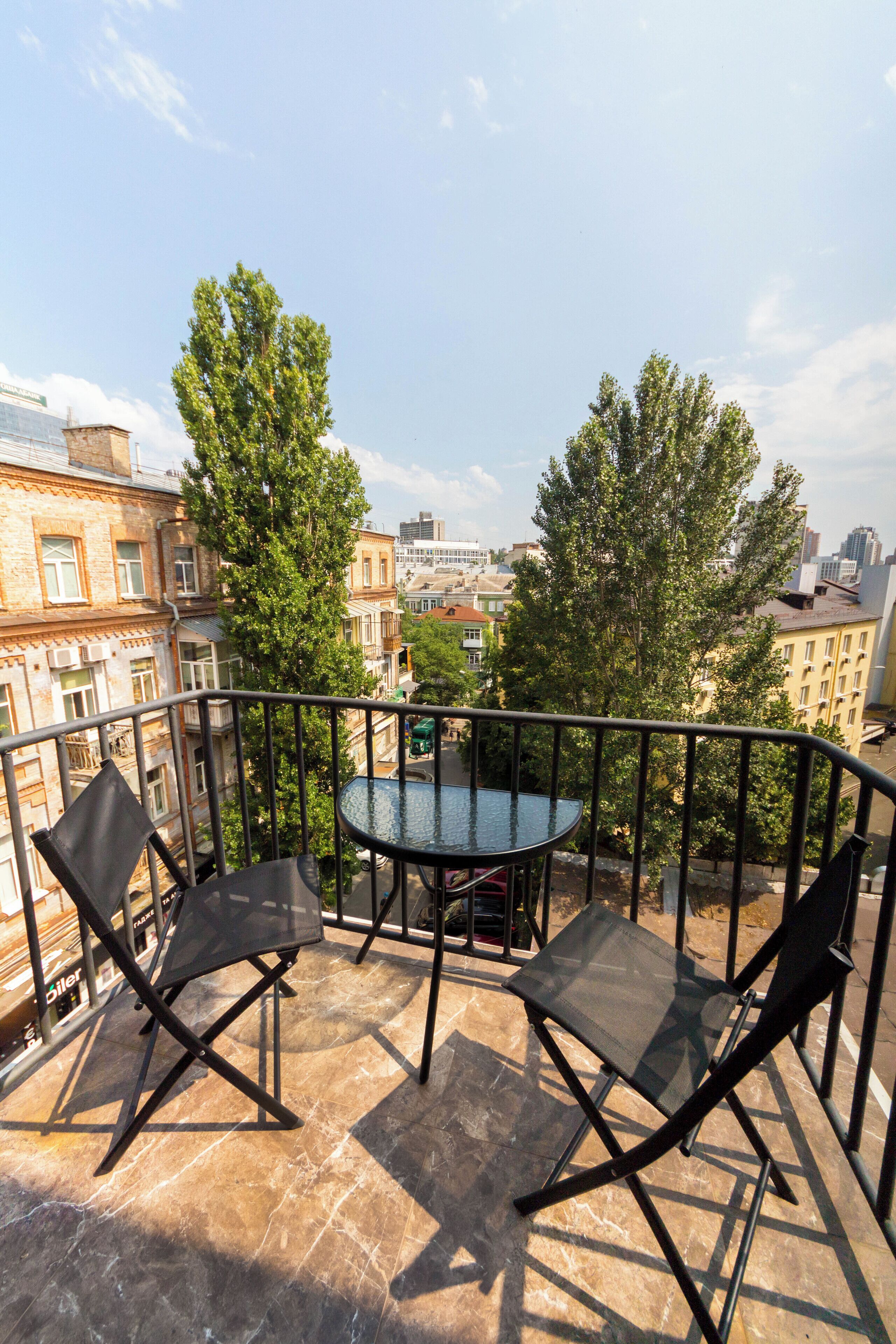 A balcony with a table and two chairs, overlooking a cityscape with buildings and trees.