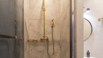 A modern shower enclosure with a glass door, a handheld showerhead, and a wall-mounted faucet.