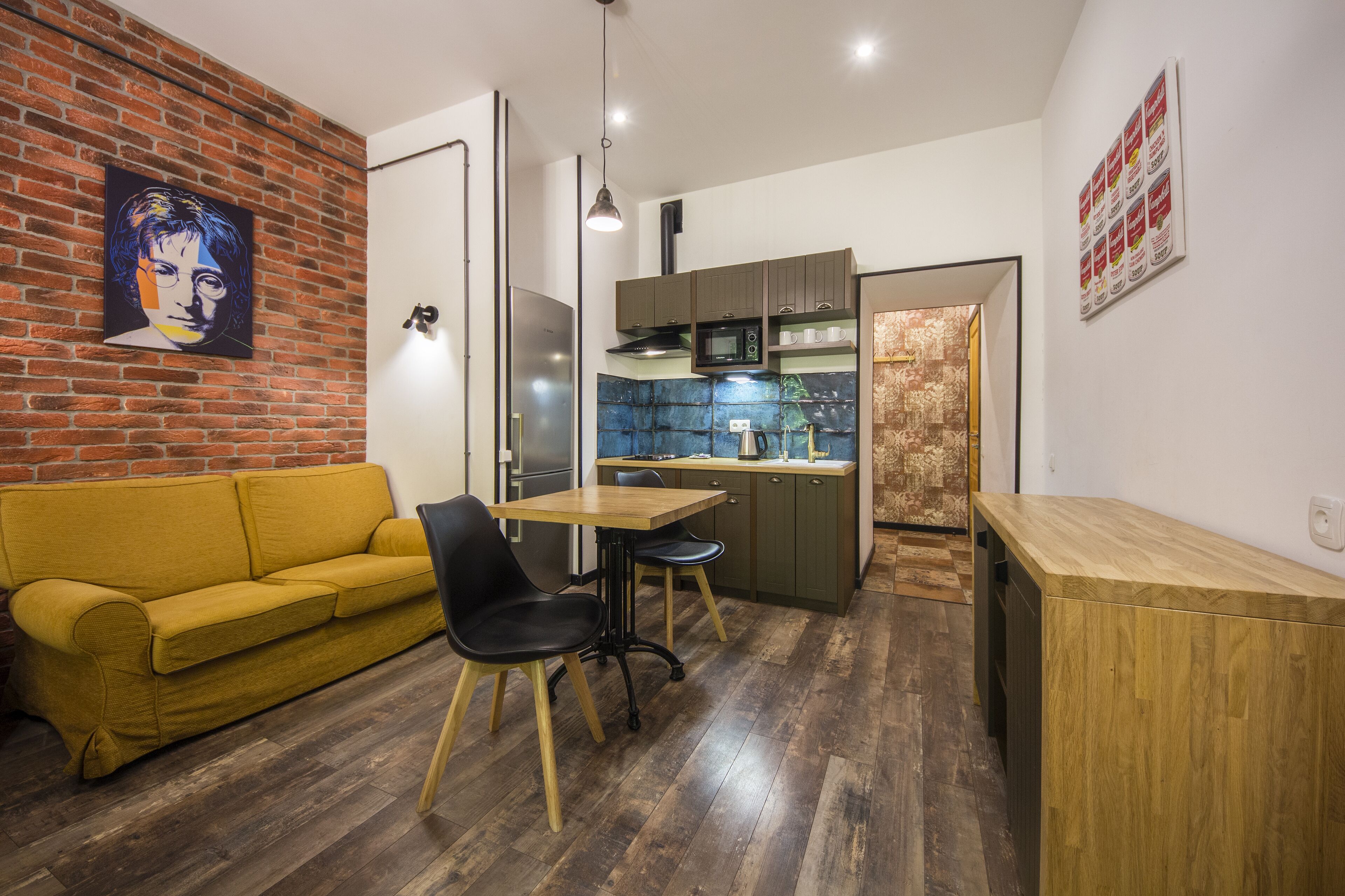 Un espacio habitable compacto con sofá, mesa de comedor, sillas, zona de cocina y pared de ladrillo.