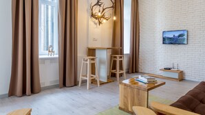 Un salon moderne avec un mur en briques blanches, une table basse en bois, un canapé marron et un téléviseur fixé au mur.