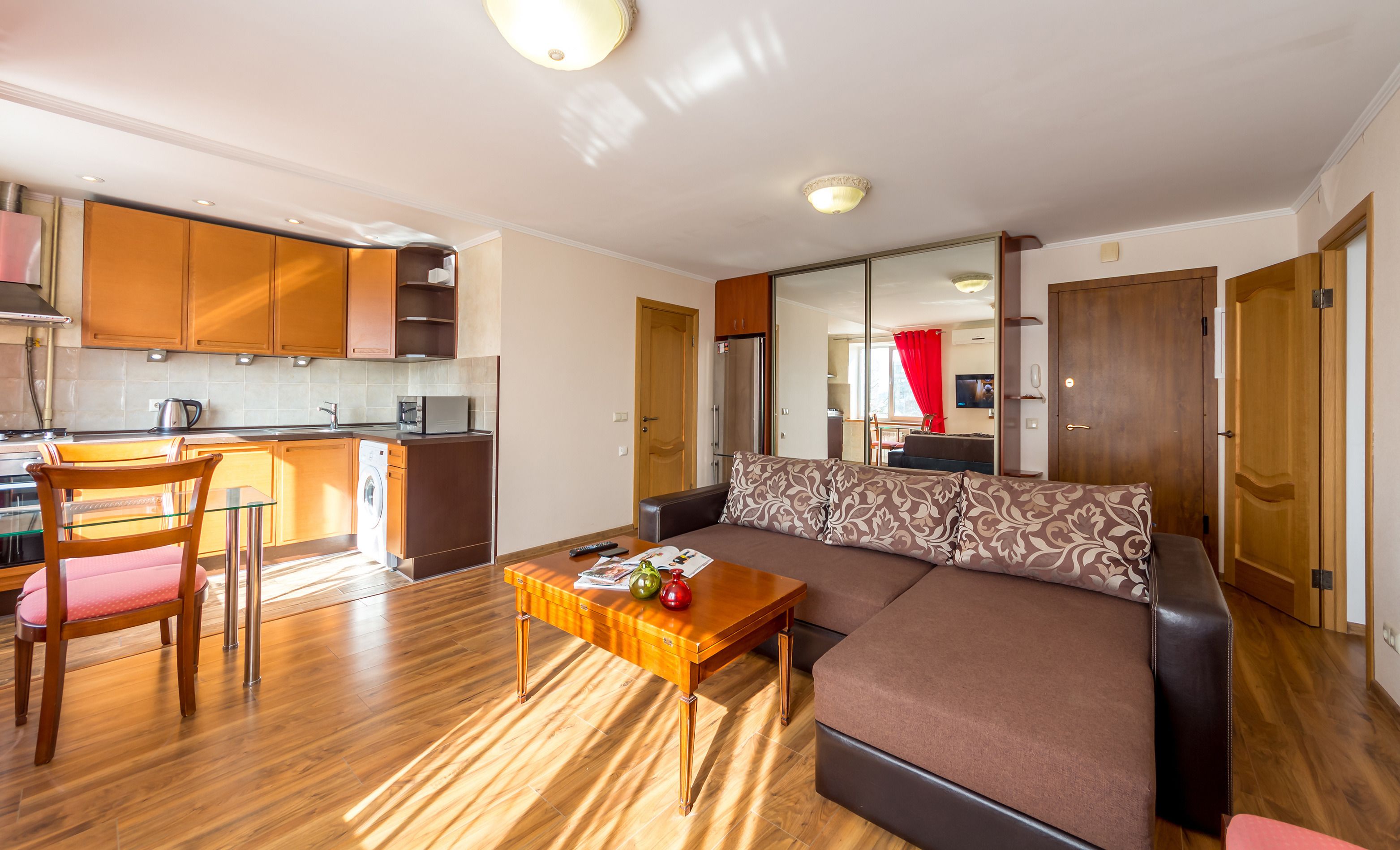 A modern living room with a sofa, a wooden coffee table, and a dining area with a chair and a washing machine.