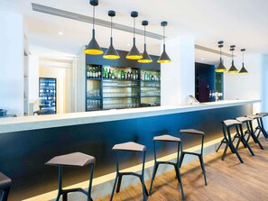 Un espace bar avec un comptoir, des tabourets, des suspensions décoratives et des étagères remplies de bouteilles et de verres.
