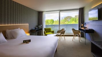 A hotel room with a large bed, a desk with a chair, a small table, and a TV mounted on the wall.