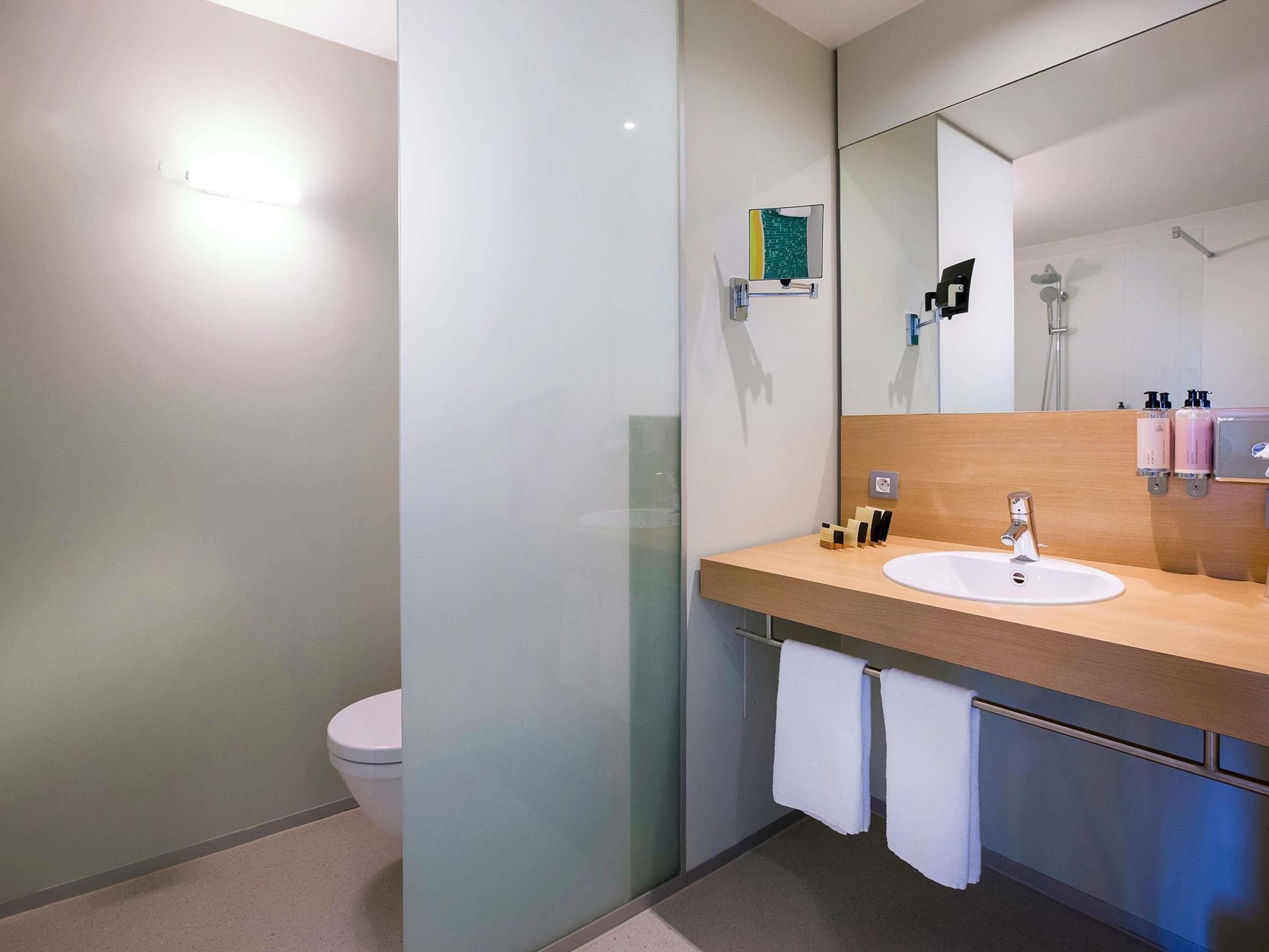 A modern bathroom with a glass shower enclosure, a wooden vanity with a white sink, and a large mirror.