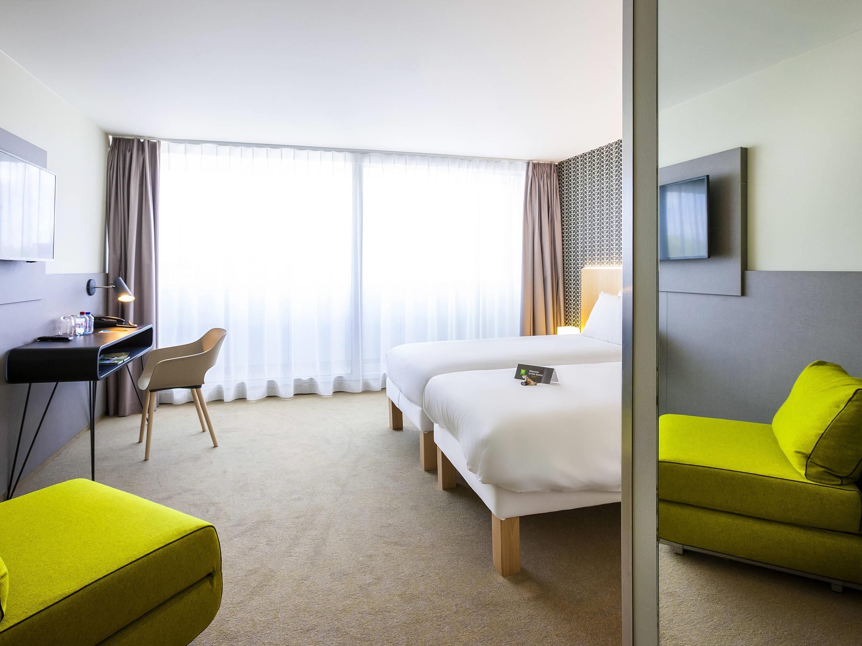 Een hotelkamer met twee bedden, een bureau met stoel, een televisie en een felgroene bank.