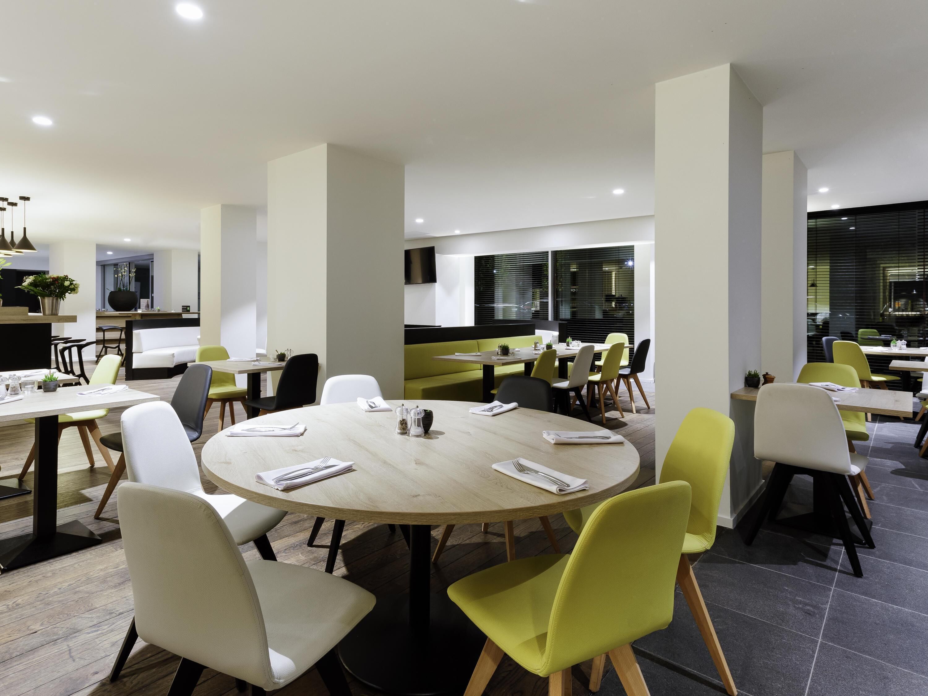 A modern dining area with round tables, chairs, and a kitchen in the background.