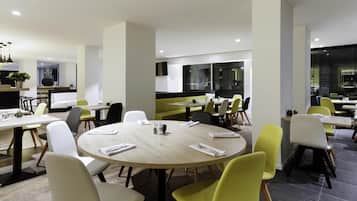 A modern dining area with round tables, chairs, and a kitchen in the background.