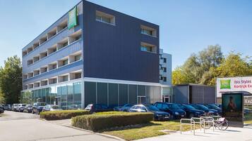 Un edificio moderno con diversi piani, ampie finestre e un’area di parcheggio con diverse auto.