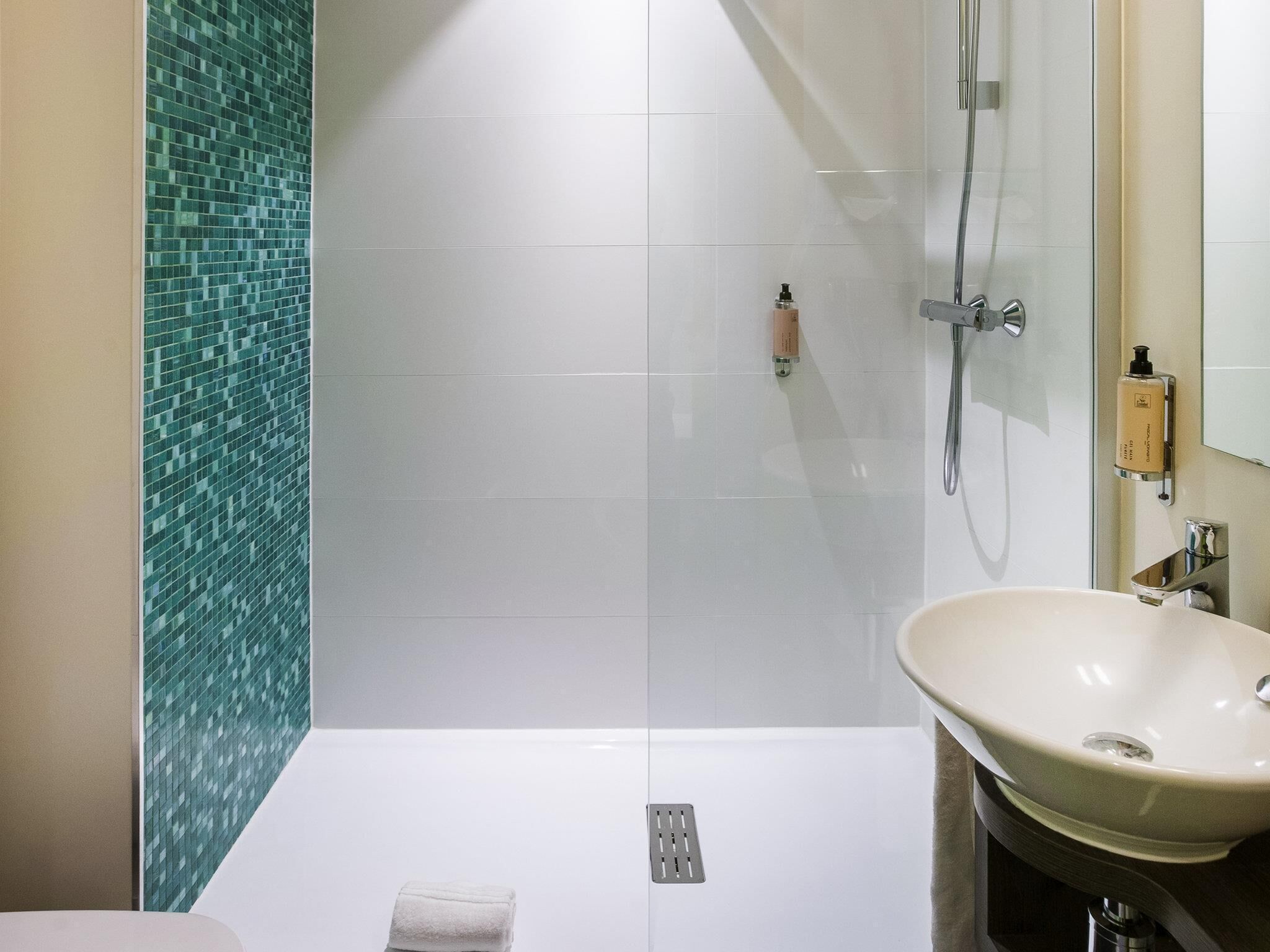Een badkamer met een douchecabine van glas, een wastafel en een spiegel.