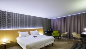 Ein Hotelzimmer mit Bett, Nachttisch, Lampe, Sesseln und Schreibtisch.