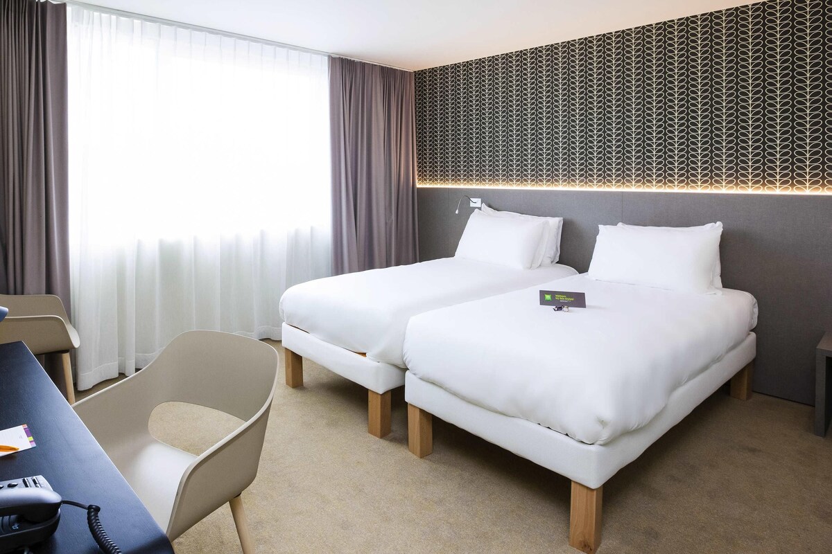 Una habitación de hotel con dos camas, un escritorio con teléfono y una pared moderna con diseño.