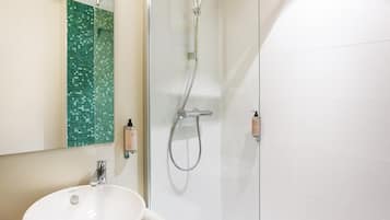 A bathroom with a white sink, a glass shower enclosure, and a green mosaic tile backsplash.